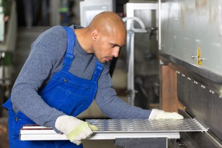 A man in blue overalls working on a metal counter.