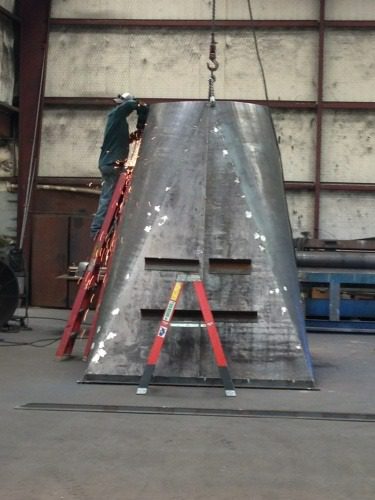 A large metal object being worked on by a crane.