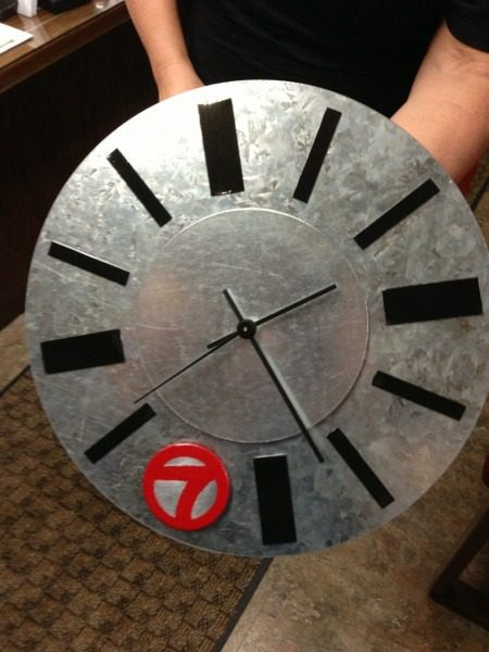 A person holding a clock with the number 7 on it.