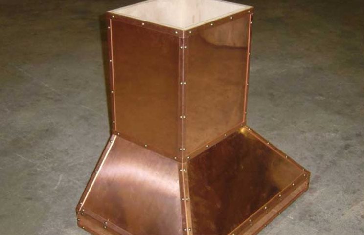 A copper stove hood sitting on top of the floor.