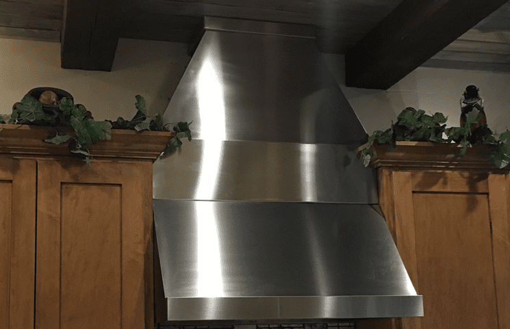 A stainless steel range hood in the middle of a kitchen created with metal fabrication.